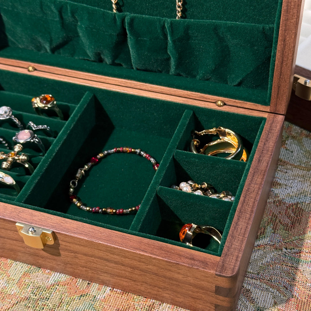Jewelry box with green interior displaying various jewelry items on a patterned fabric background.