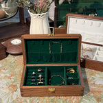 Wooden jewelry box with green interior displaying various jewelry items on a floral background.